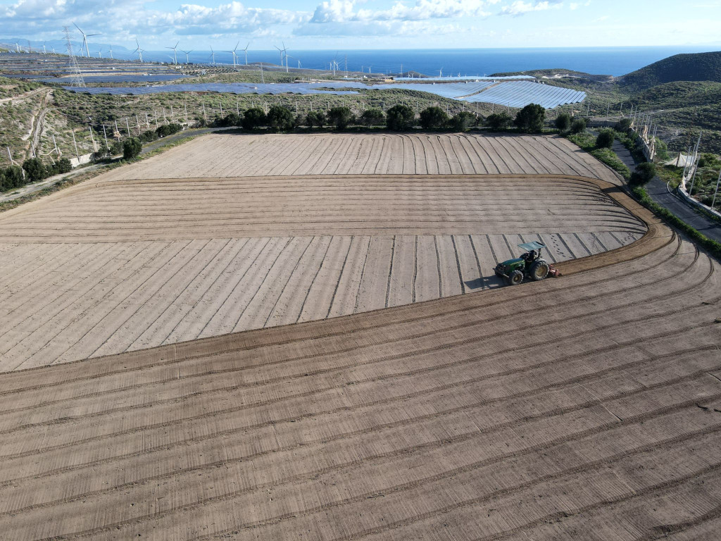 Ploughed field with tractor in the background, windmills and sea in Tenerife.