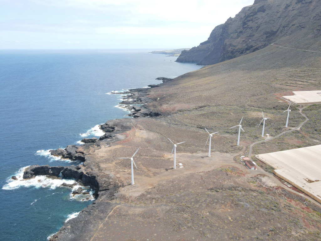 Wind turbines on the coast of Tenerife next to cliffs and sea.