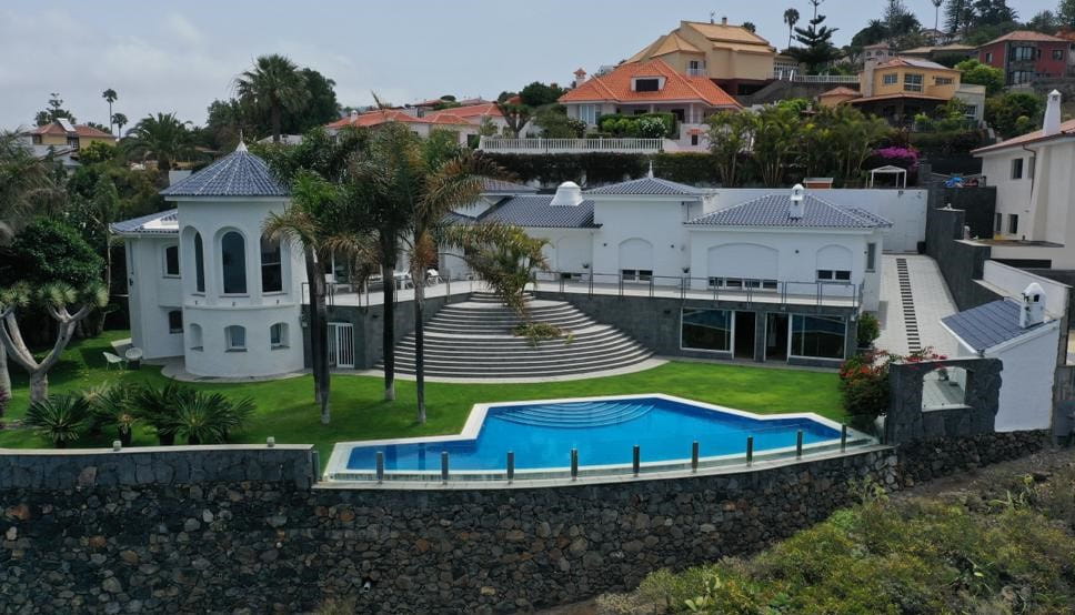 Modern villa with pool and garden in Tenerife, surrounded by houses and palm trees.