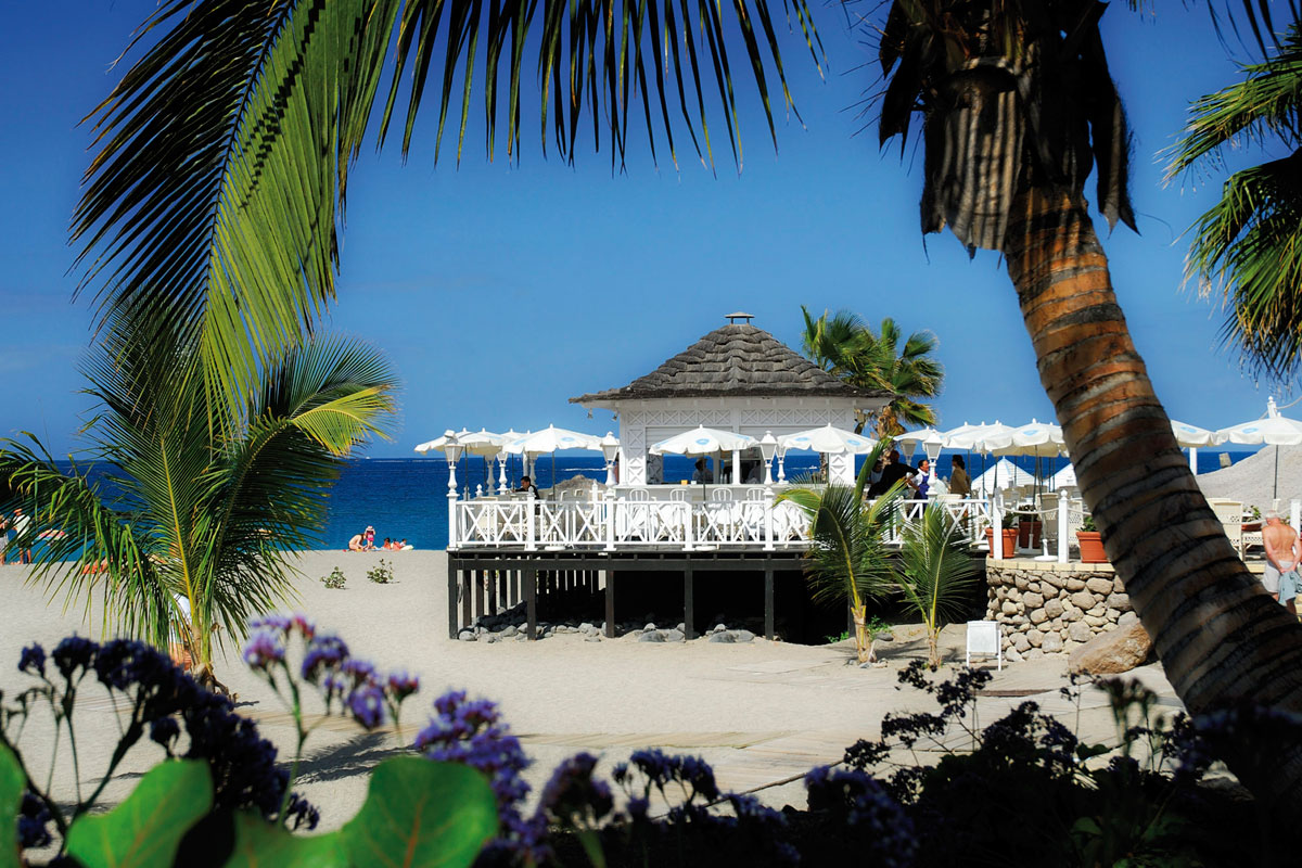 White kiosk on the beach with palm trees and blue sea in Tenerife.