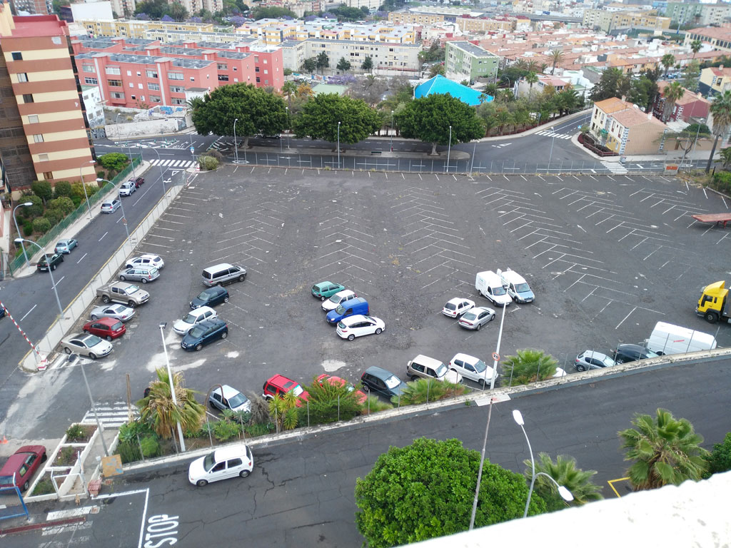 Semi-empty parking in Puerto de la Cruz, Tenerife, with cars and buildings around.