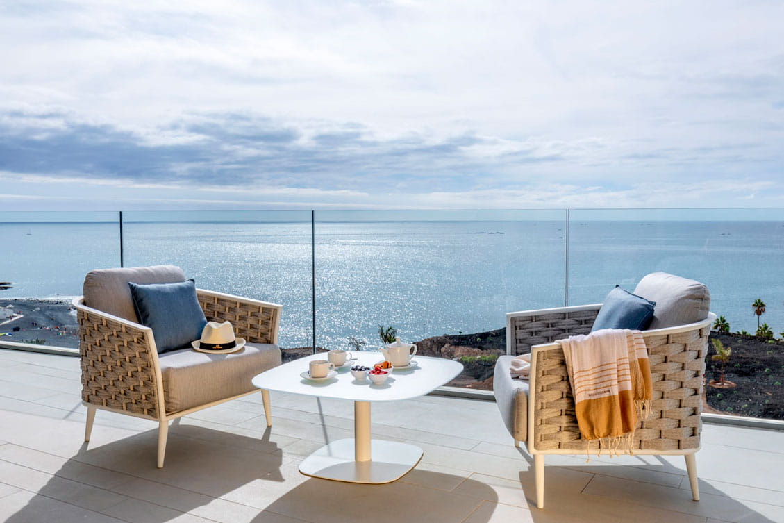 Terrace with chairs and table facing the sea in Tenerife, blue background and cloudy sky.