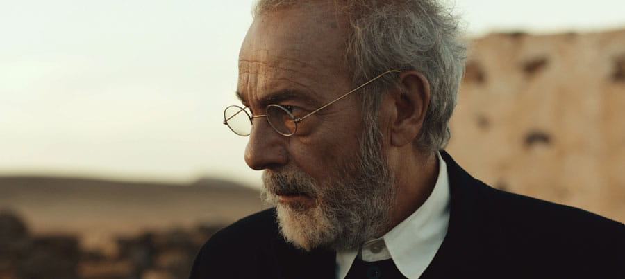 A man with glasses and a beard looking to the right in an arid environment.