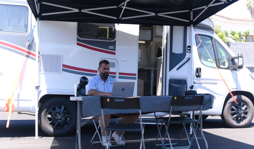 Person working on laptop under awning next to caravan in Tenerife.