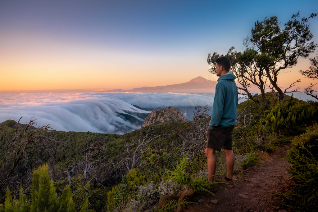 Man standing on trail overlooking Teide mountain and clouds at sunset in Tenerife.