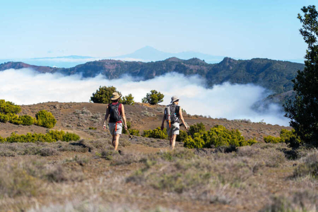 Two hikers walking on a trail with mountains and clouds in the background, Tenerife.
