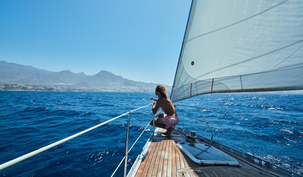 Person sailing and enjoying the view of Tenerife coastline from a yacht.