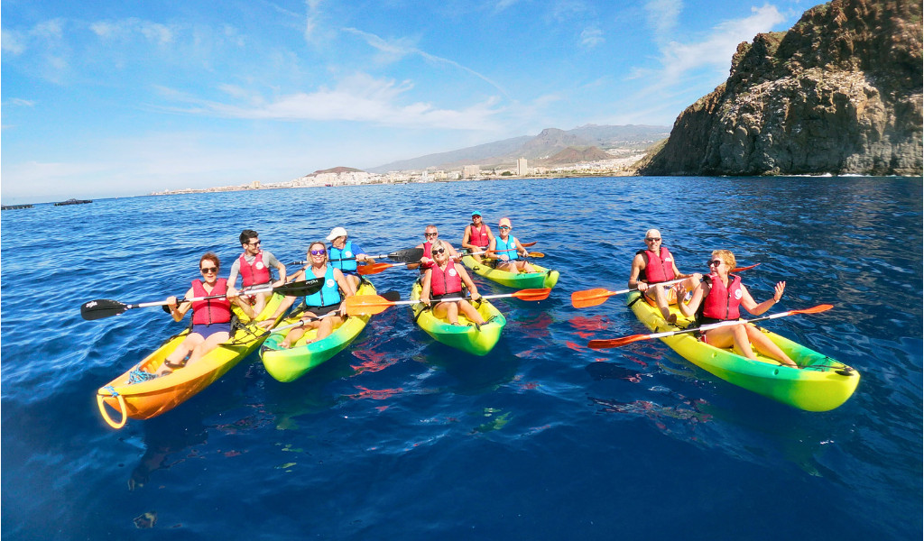 Group kayaking on blue sea near cliffs in Tenerife.