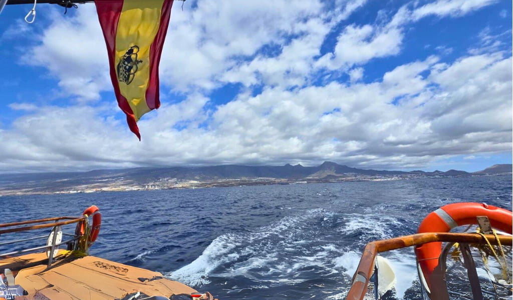 Boat sailing near the coast of Tenerife with Spanish flag and mountains in view.