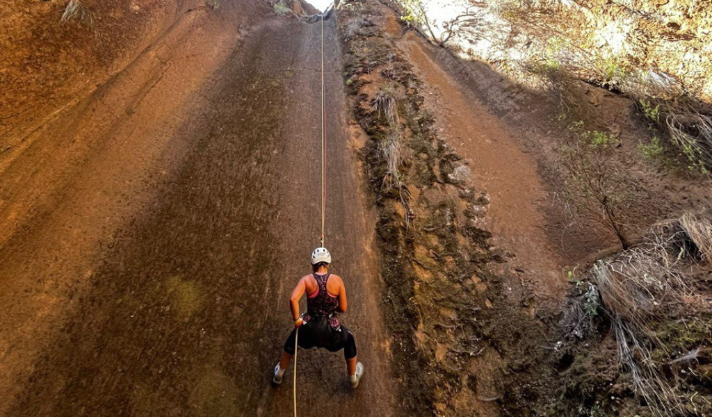 Person abseiling down a steep canyon wall in Tenerife, wearing a helmet and harness.