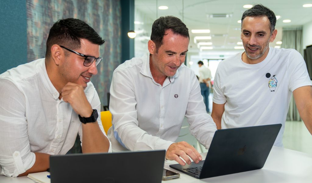 Three men collaborating on a laptop in an office in Tenerife.