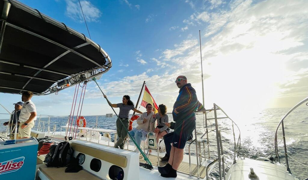 People sailing on a yacht in Tenerife with a Spanish flag at sunset.