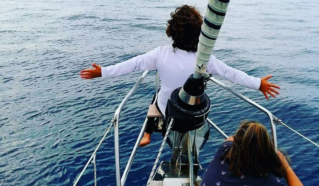 Child on sailboat bow with arms outstretched over the ocean near Tenerife coast.