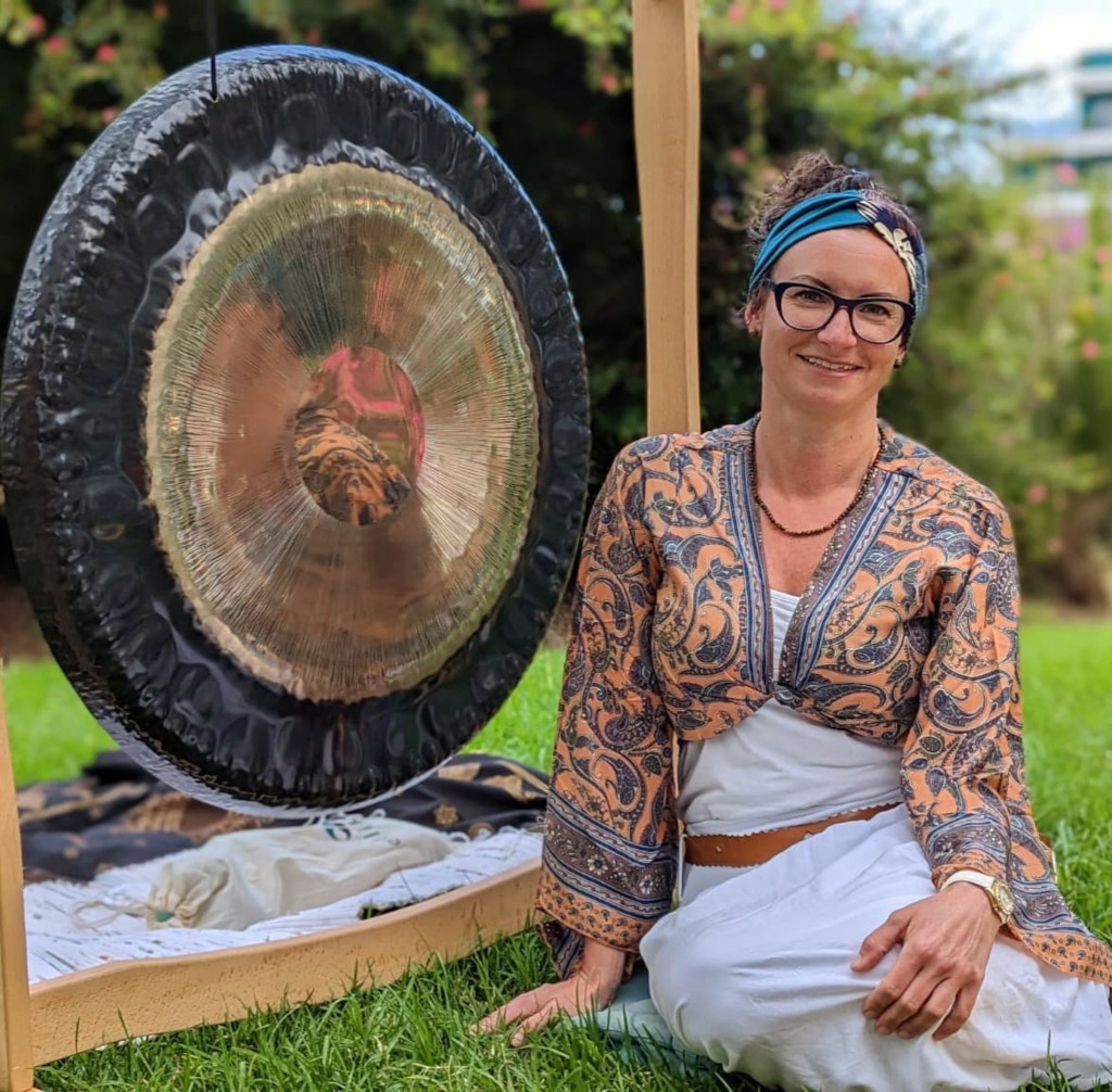 Woman sitting on grass beside a large gong, smiling in a park in Tenerife.