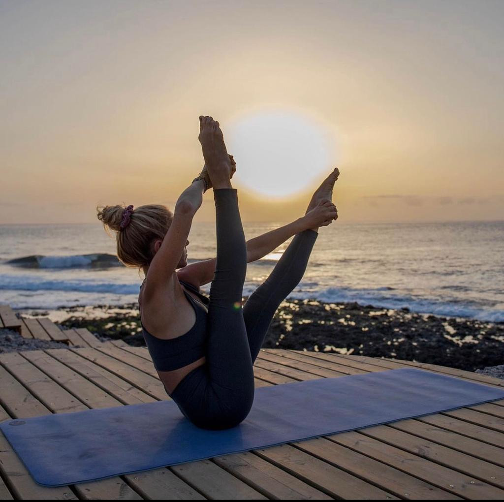 Person practicing yoga on a mat by the ocean at sunset in Tenerife.