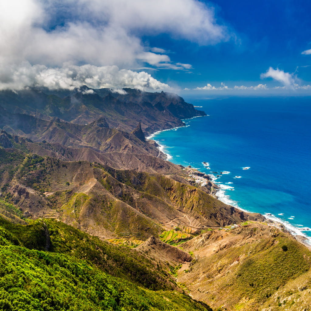 Rugged coastline and mountains of Tenerife under a cloudy sky, meeting the blue ocean.