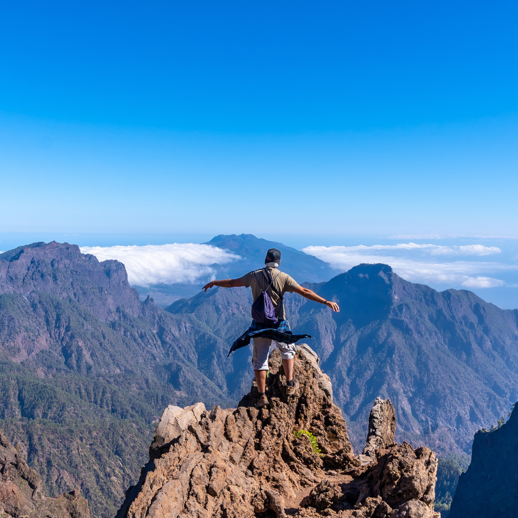 Person standing on rocky peak with arms outstretched, overlooking mountains in Tenerife.