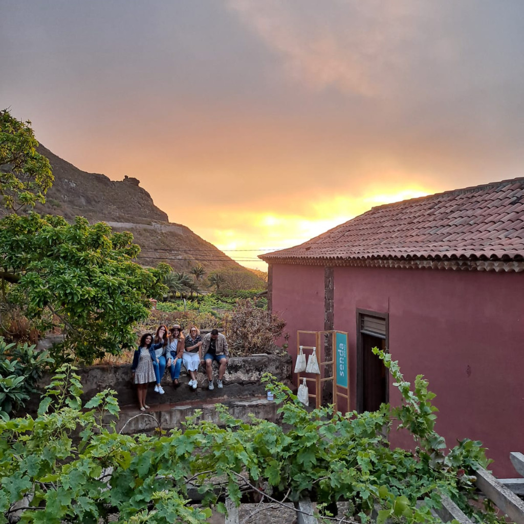 Group of people sitting on a wall at sunset near a red house in Teno, Tenerife.