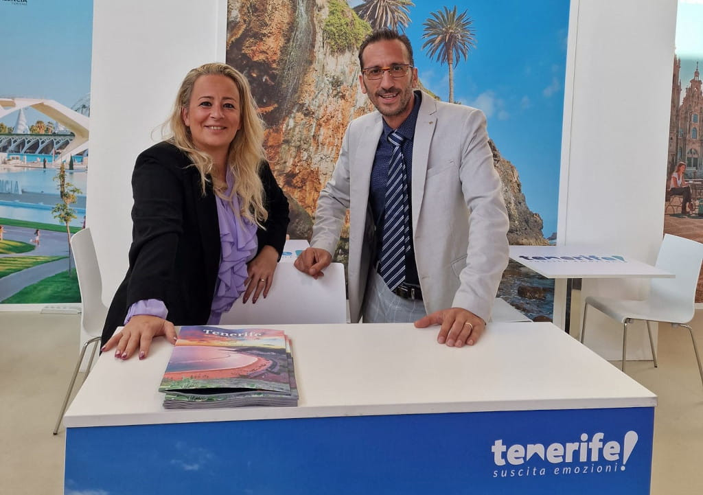 Two people smiling at a promotional stand for Tenerife with brochures on the table.