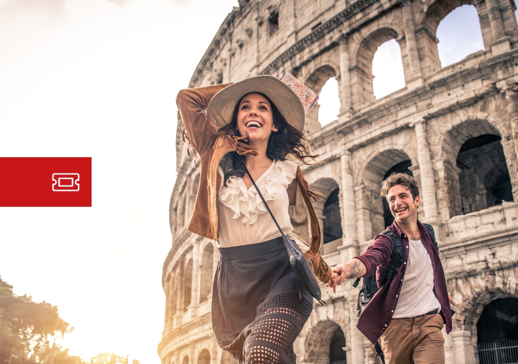 Smiling tourist couple running in front of the Colosseum in Rome at sunset, with backpacks and casual clothing.