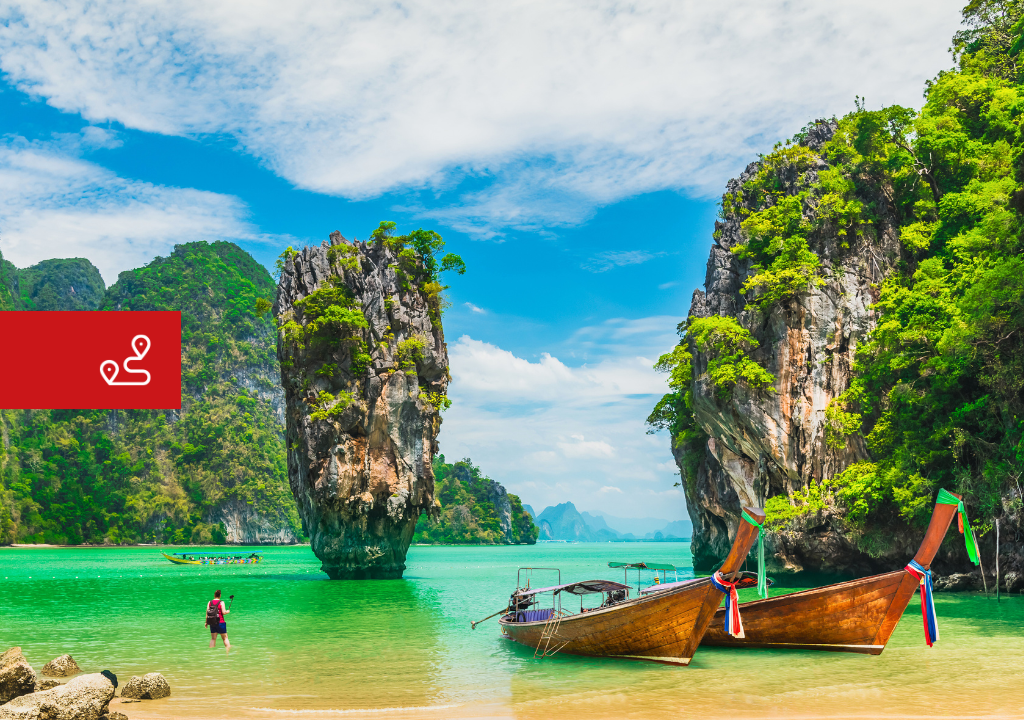 Tropical beach with wooden boats on turquoise water and large vegetation-covered rock formations.