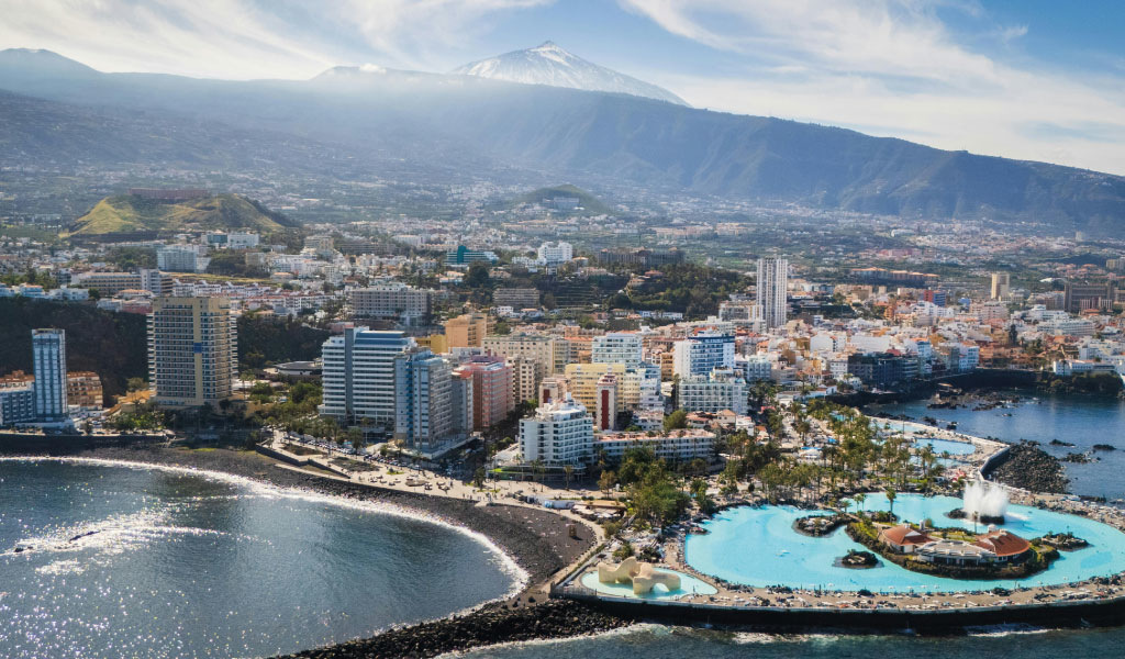 Aerial view of Puerto de la Cruz, Tenerife, with coastline and tall buildings.