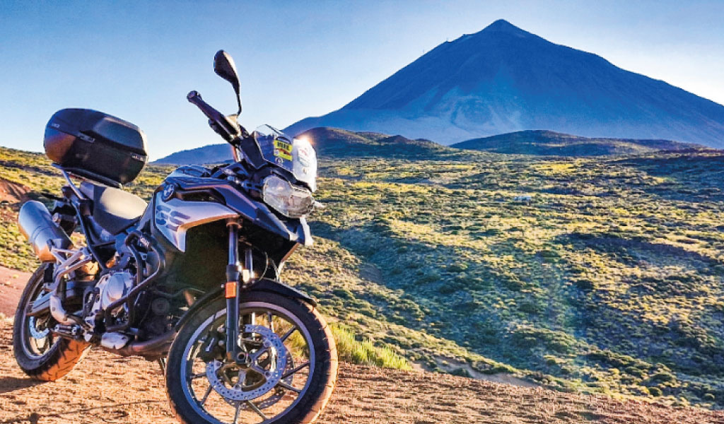 Motorcycle parked in front of Mount Teide in Tenerife under blue skies.
