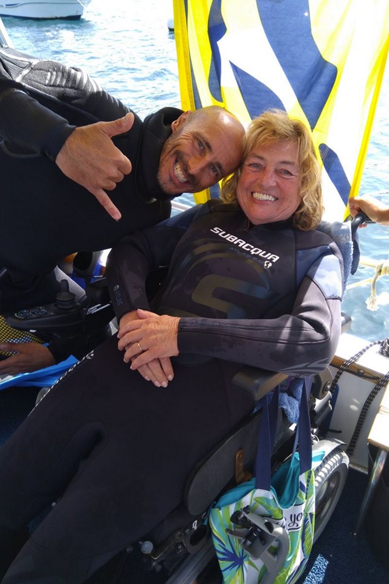 People in smiling diving suits in a wheelchair near the sea in Tenerife.
