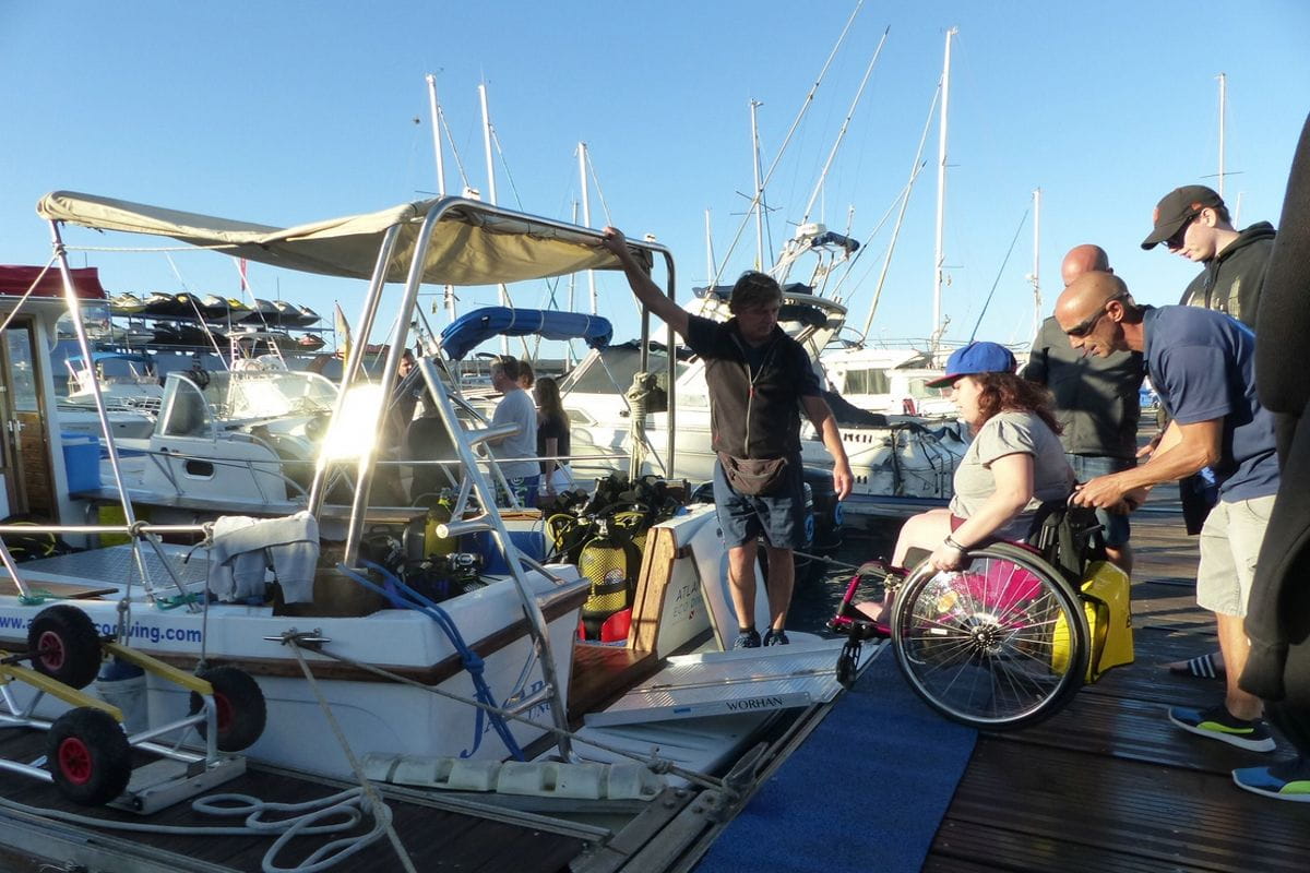 Person in a wheelchair boarding a boat in Tenerife with the help of several people.