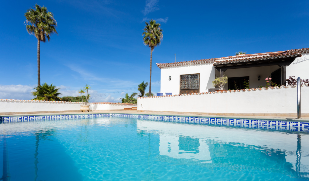 Swimming pool and house with palm trees in Tenerife under blue skies.