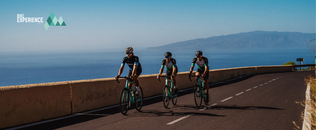 Cyclists on the road with ocean and views of Tenerife. Text: Bike Experience.