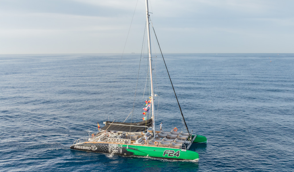 Catamaran sailing on the ocean near Tenerife, with sails and colorful flags.