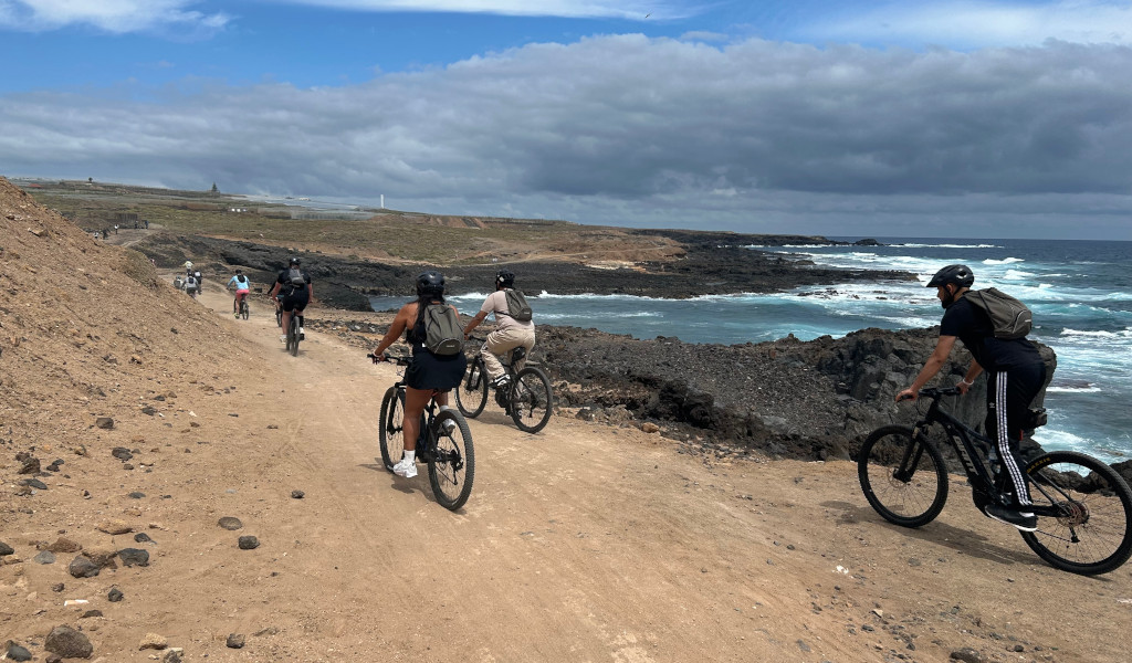 Cyclists riding along a coastal path in Tenerife by the sea and cloudy skies.