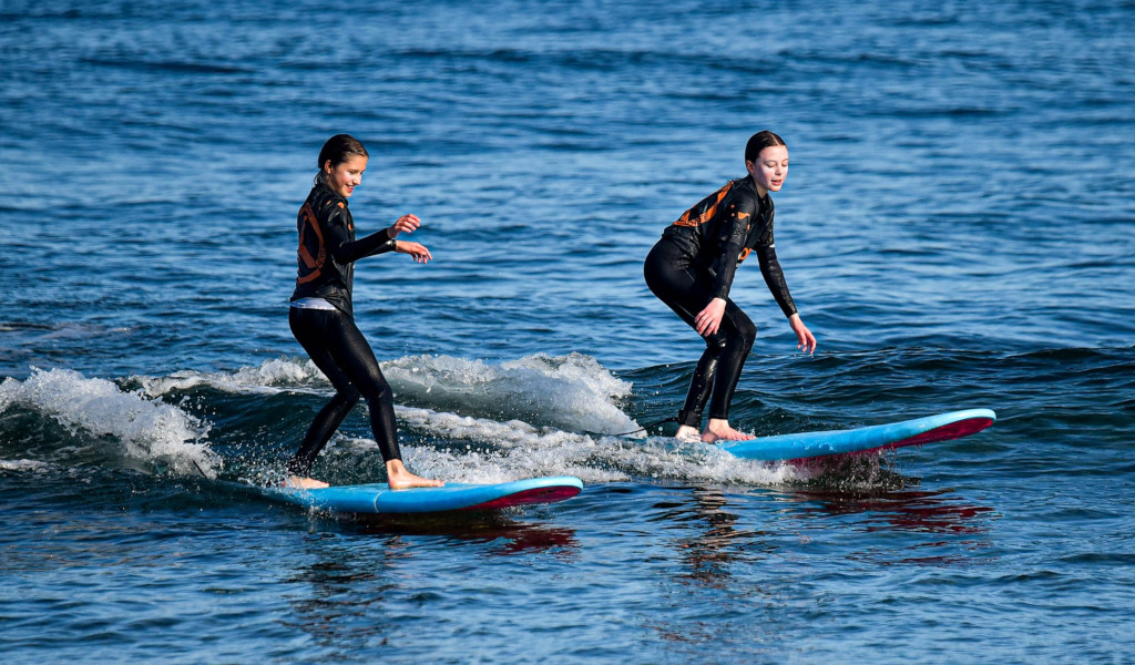 Two people in wetsuits surf small waves in the sea of Tenerife.
