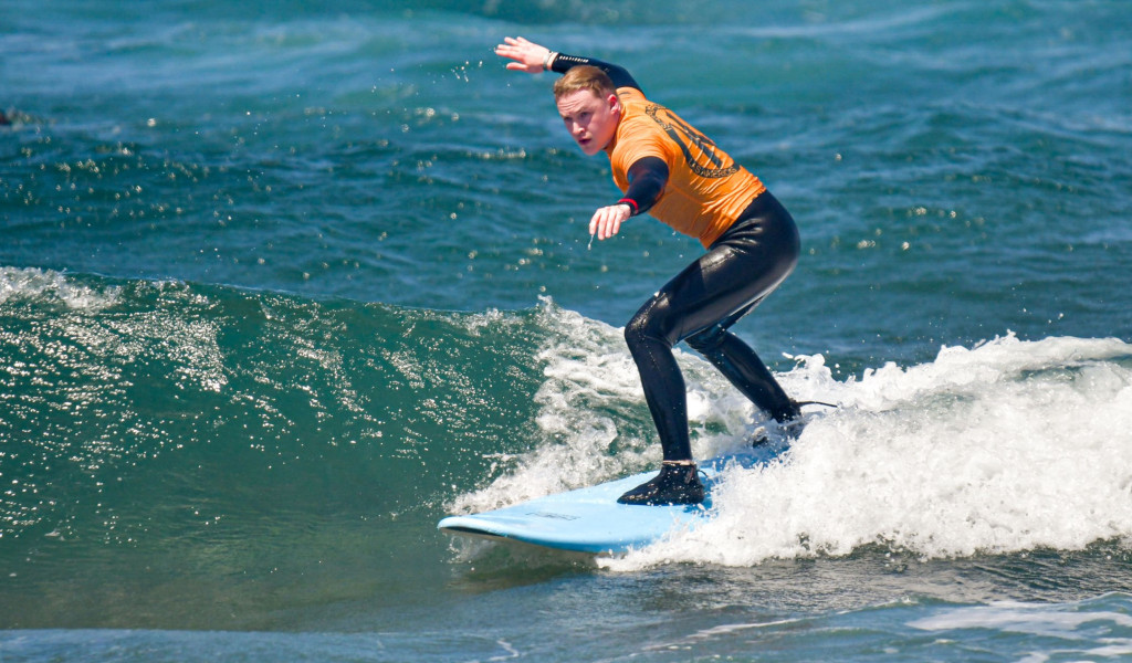 Person surfing a wave in Tenerife, wearing orange wetsuit.