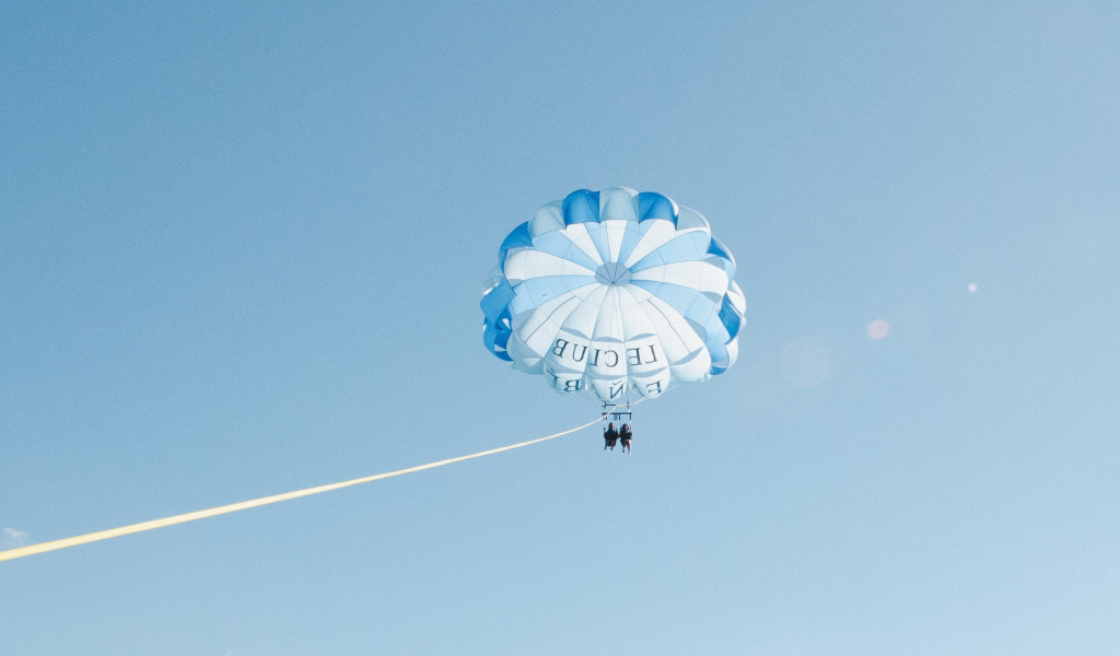 Parasailing over the sky of Tenerife with people under white and blue parachutes.