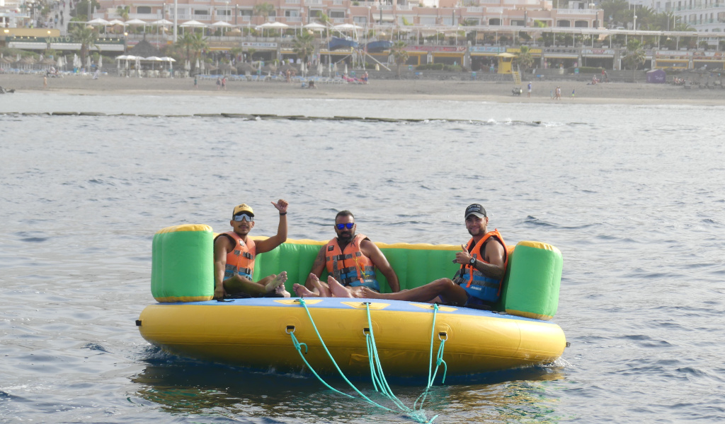 Three people on an inflatable platform in the sea, Playa de las Americas in the background, Tenerife.