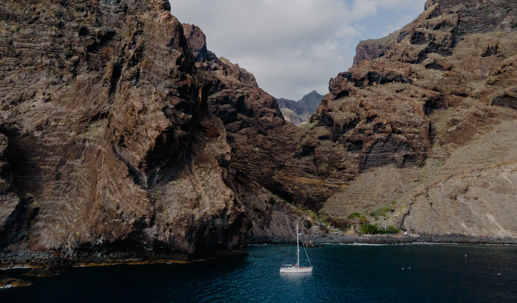 Sailboat on the rocky coast of Tenerife with blue waters and mountains in the background.
