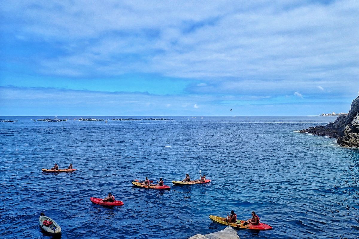Several people kayaking on the coast of Tenerife under partly cloudy skies.