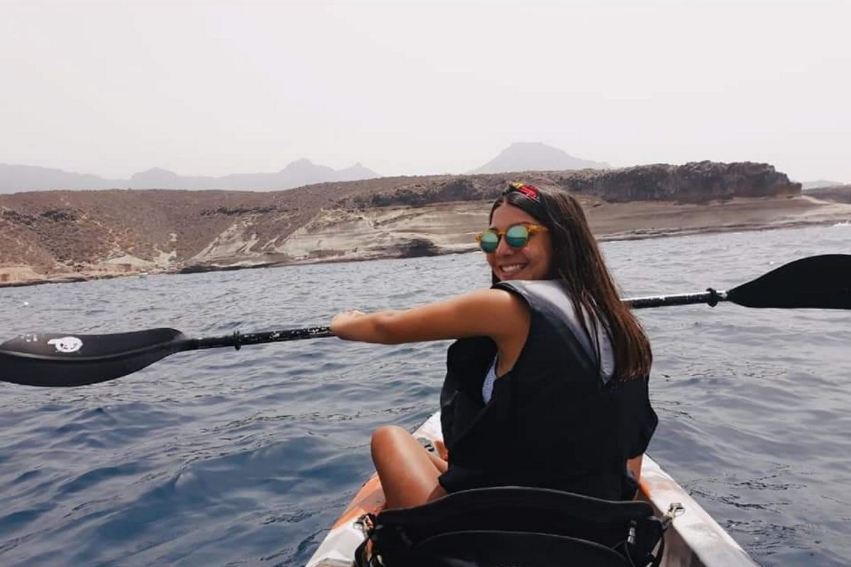 Person paddling a kayak in the waters of Tenerife, with mountainous landscape in the background.