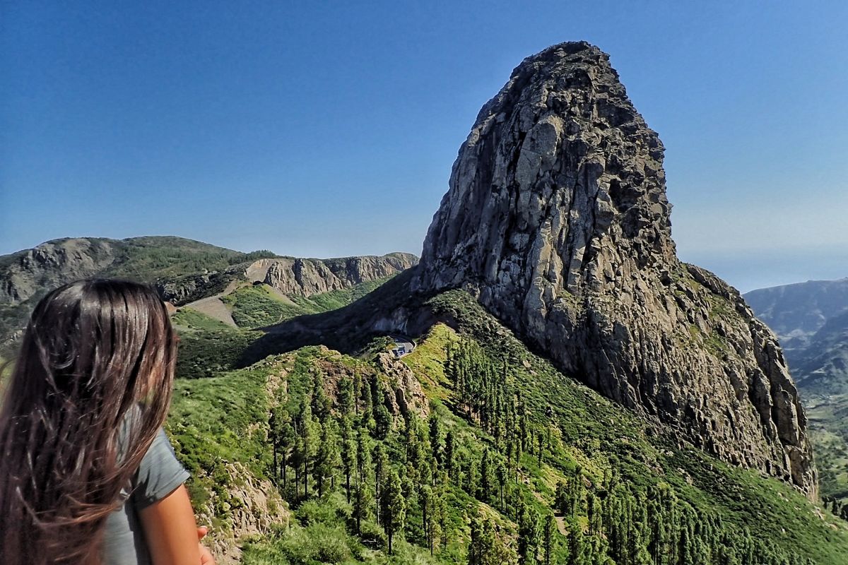 Woman observing the Roque de Agando in Tenerife, surrounded by vegetation.