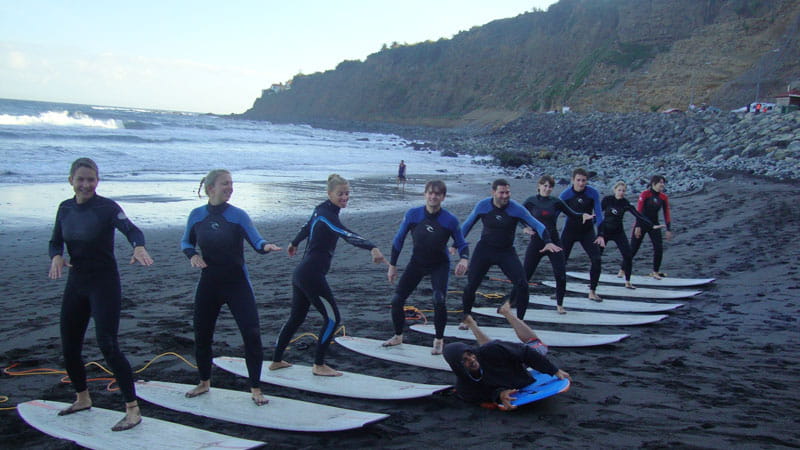 Group of people learn to surf on the beach in Tenerife, lined up on boards.