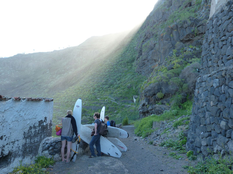 People with surfboards walking along a trail in Tenerife, surrounded by mountains.