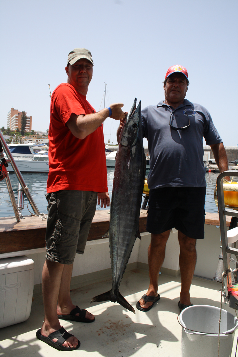 Two people on a boat holding a large fish in Los Cristianos, Tenerife.