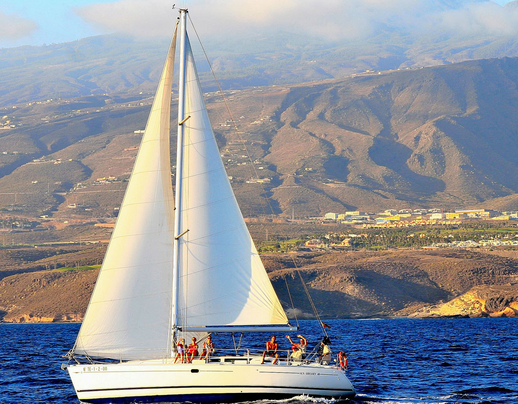 Sailboat sailing near the coast of Tenerife with mountains in the background.