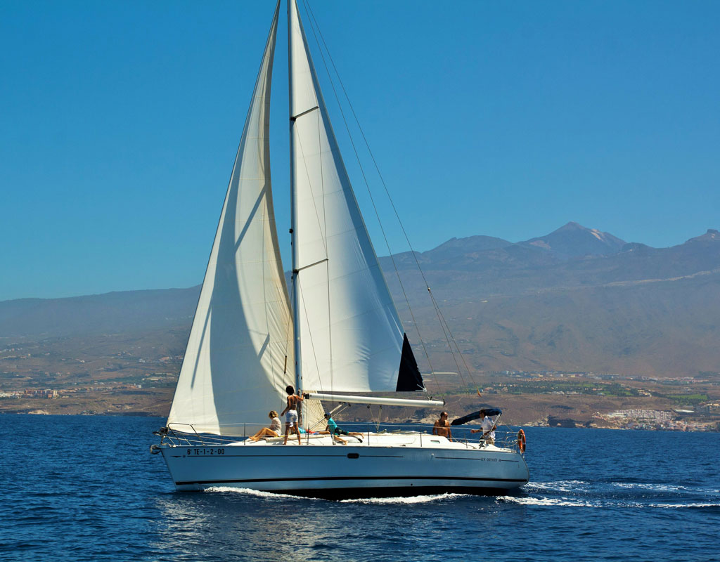 Sailboat sailing off the coast of Tenerife with mountains in the background.