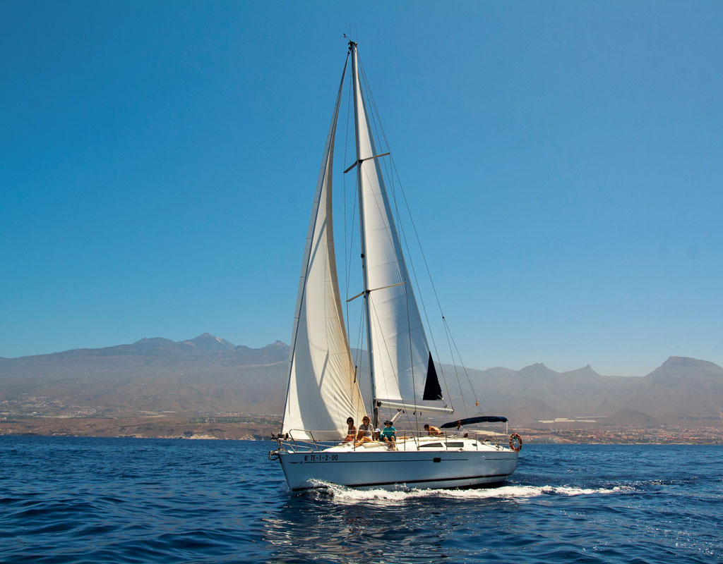 Sailboat sailing off the coast of Tenerife with mountains in the background.