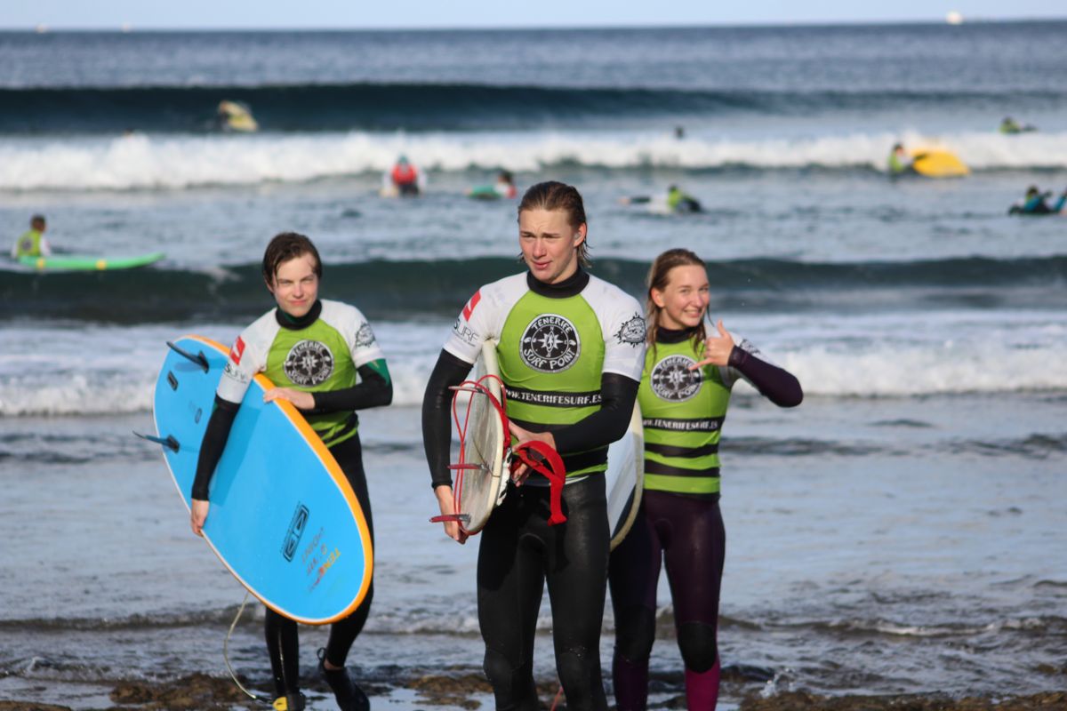 Surfers on the beach in Tenerife, with boards and wetsuits, near the sea.