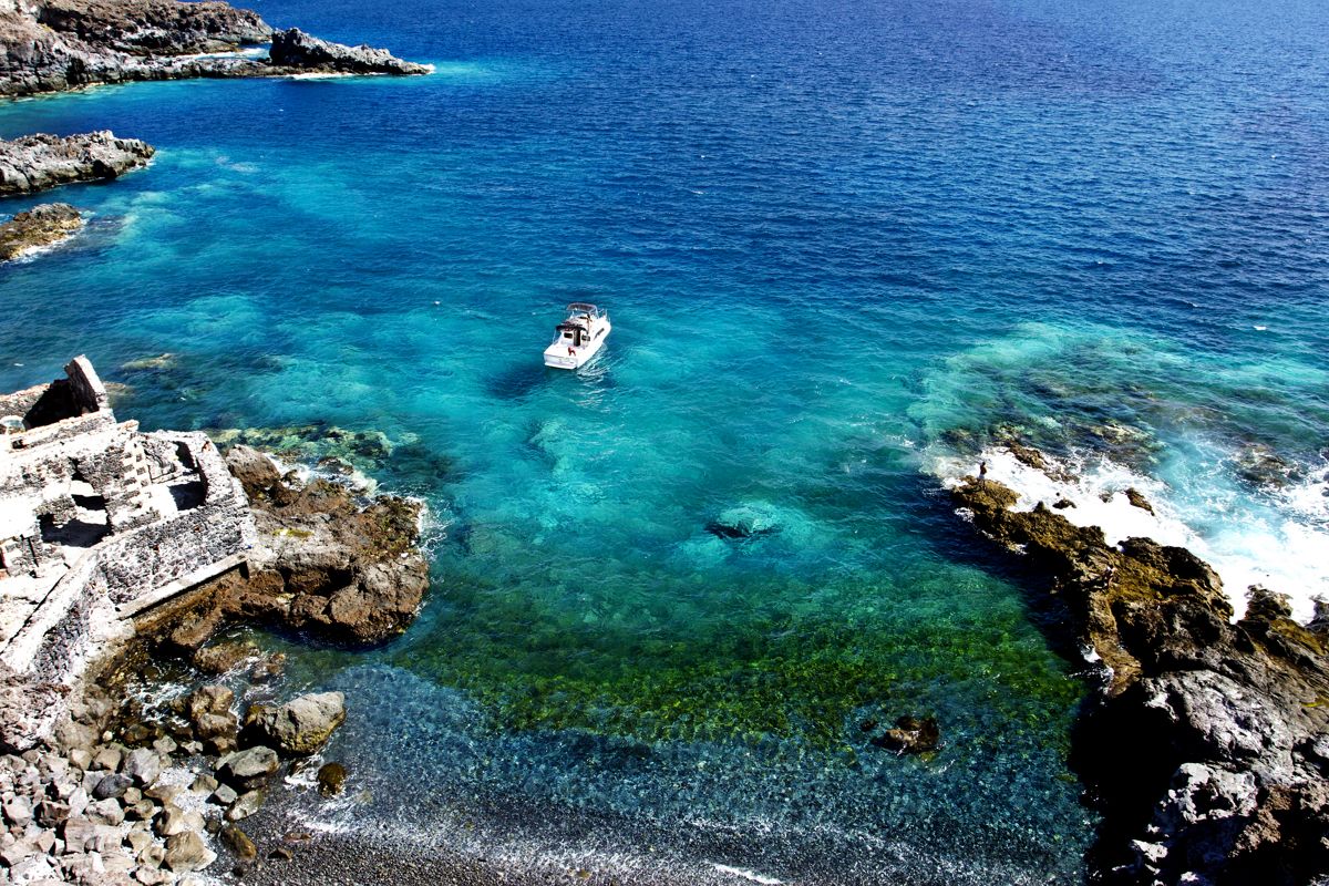Boat sailing in crystal clear waters near the rocky coast of Tenerife.