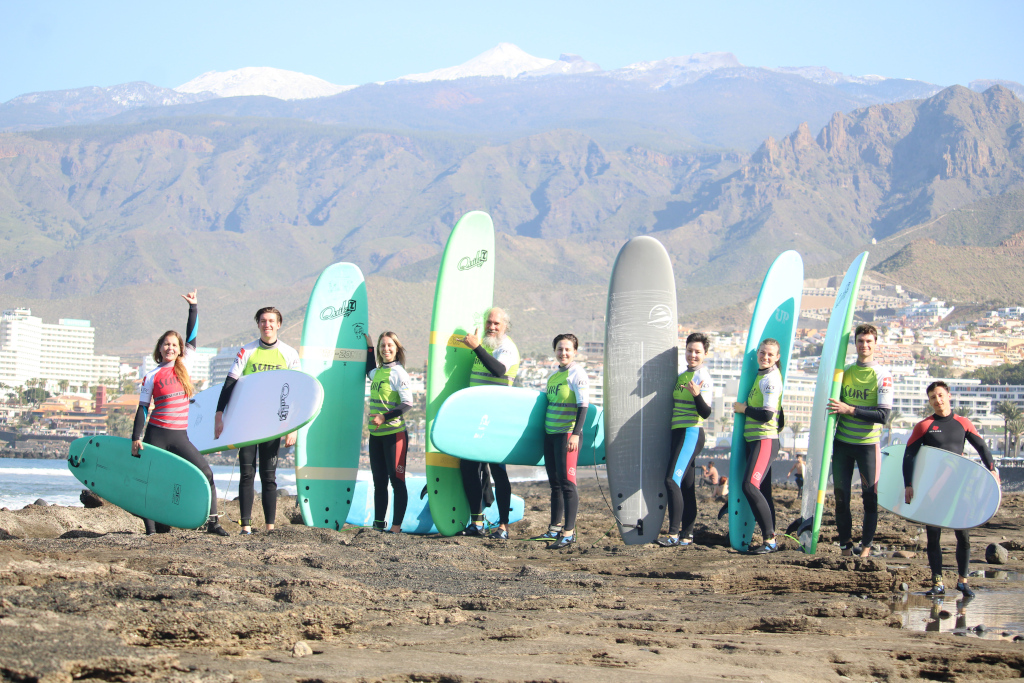 Group of surfers with boards on the beach of Tenerife, mountains in the background.